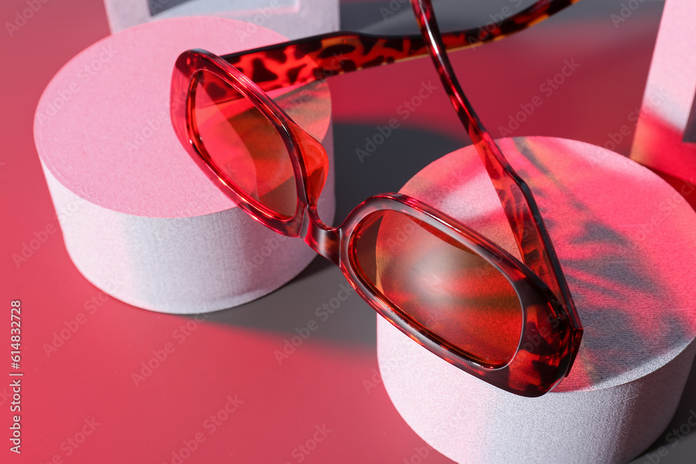 Podiums with stylish sunglasses on red background