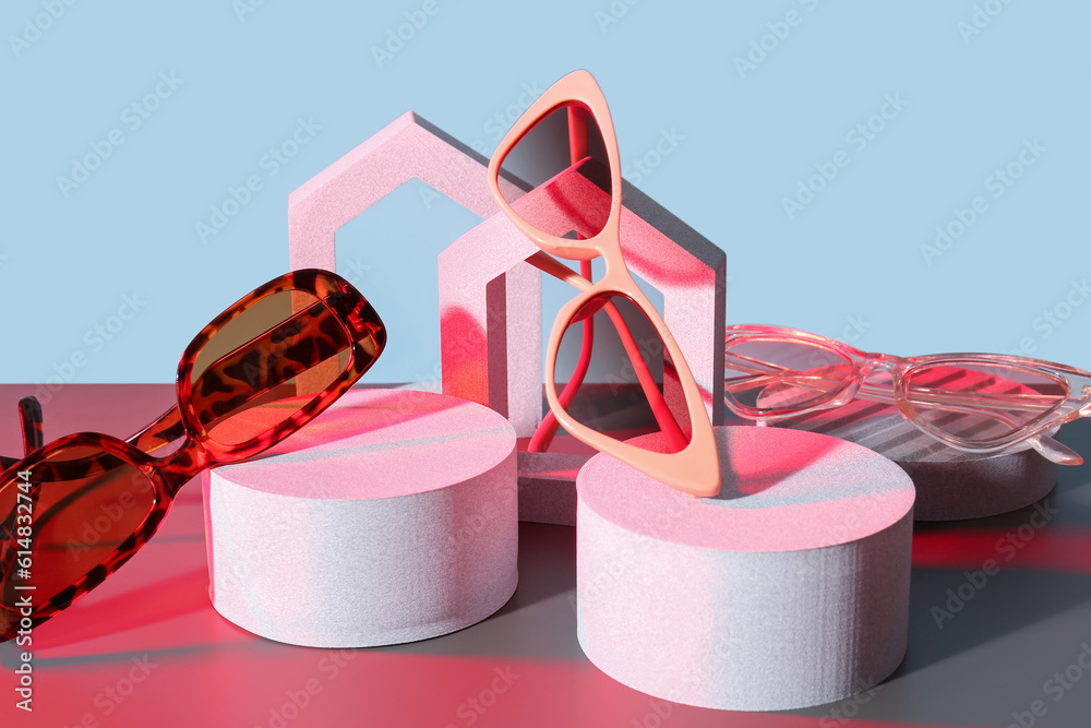 Podiums with different stylish sunglasses on colorful background