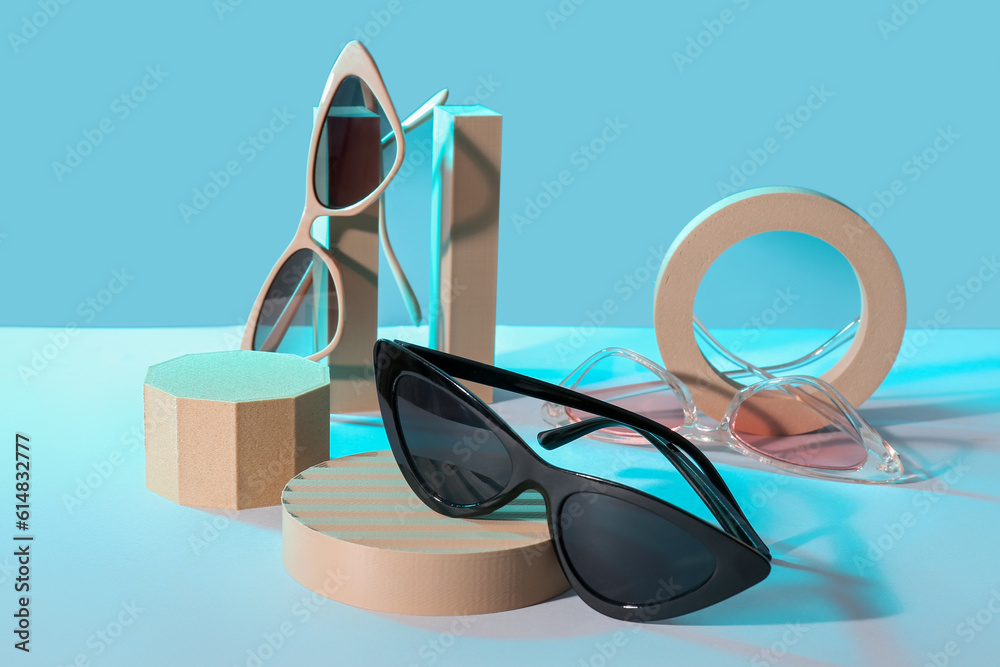 Podiums with different stylish sunglasses on blue background