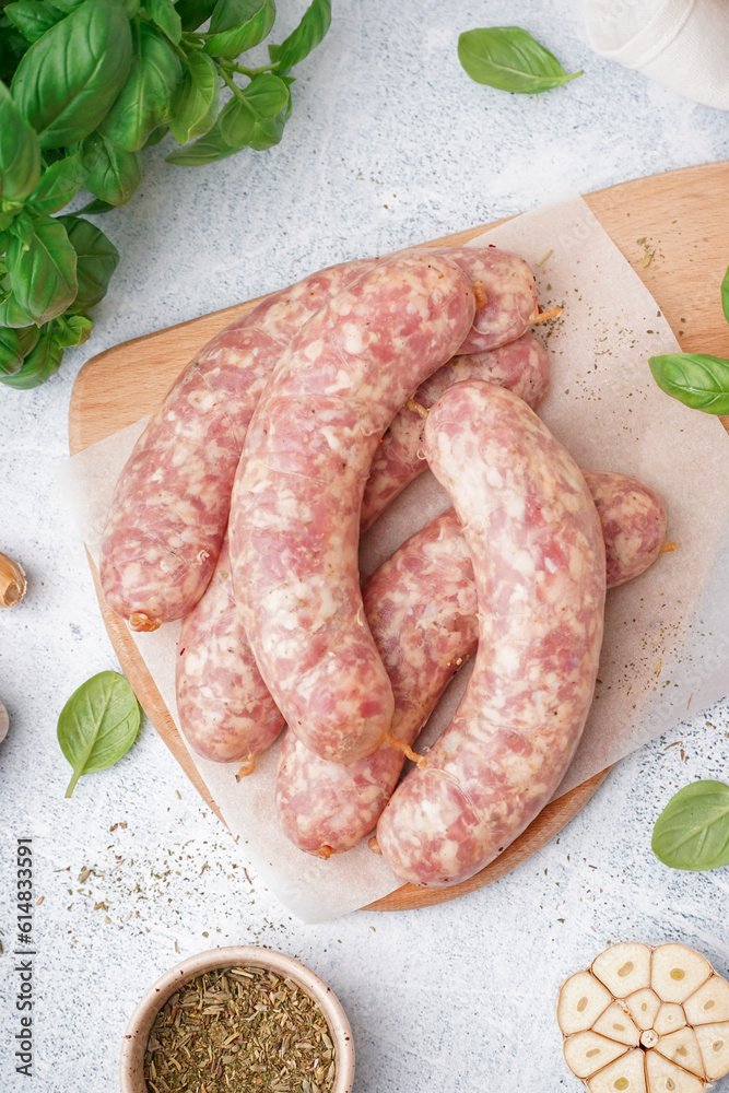 Wooden board with raw homemade sausages on light background