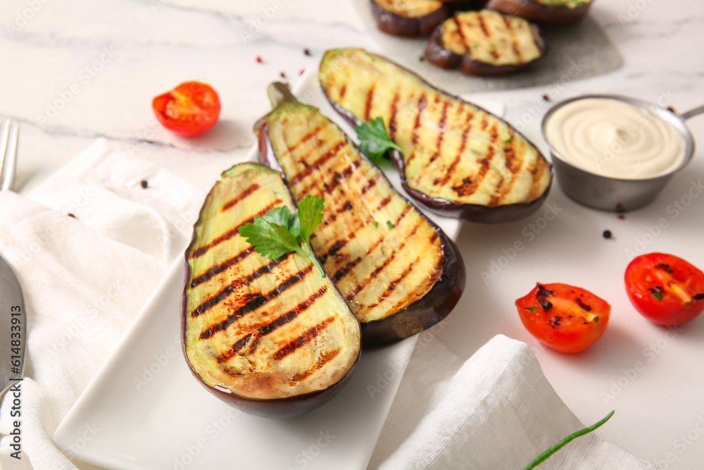 Plate with delicious grilled eggplants, sauce and tomatoes on light background