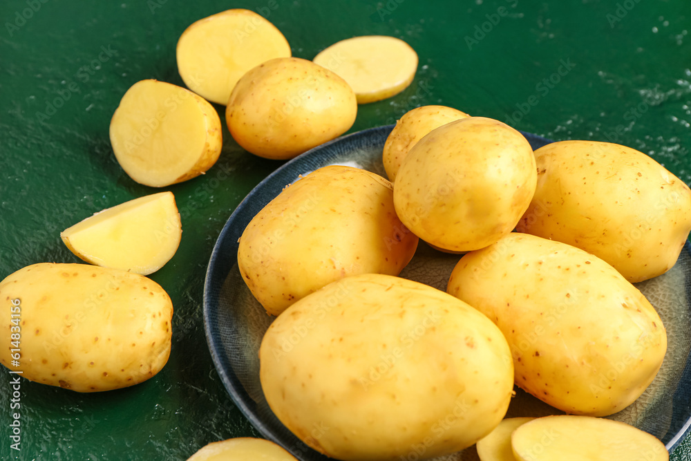 Plate with raw baby potatoes on green background