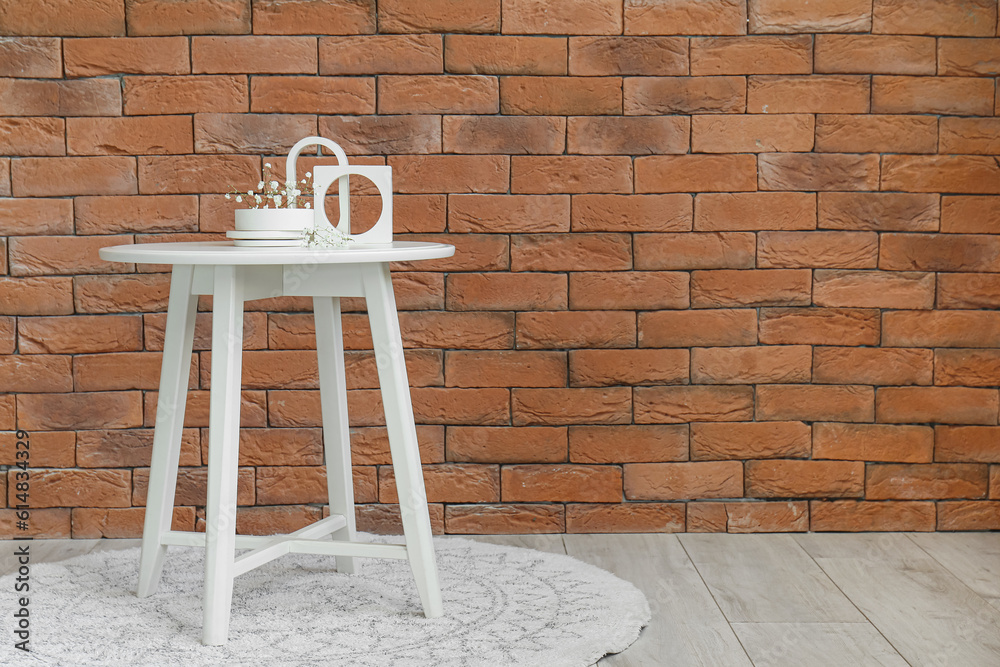 Gypsophila flowers and candle on table near brick wall in room