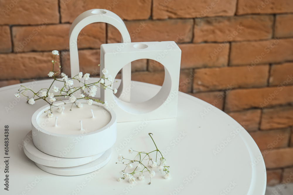 Gypsophila flowers and candle on table near brick wall in room, closeup