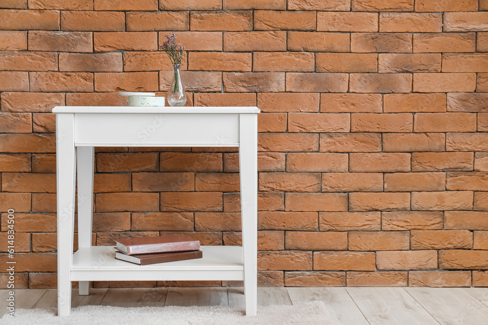 Beautiful flowers, books and candle on table near brick wall in room