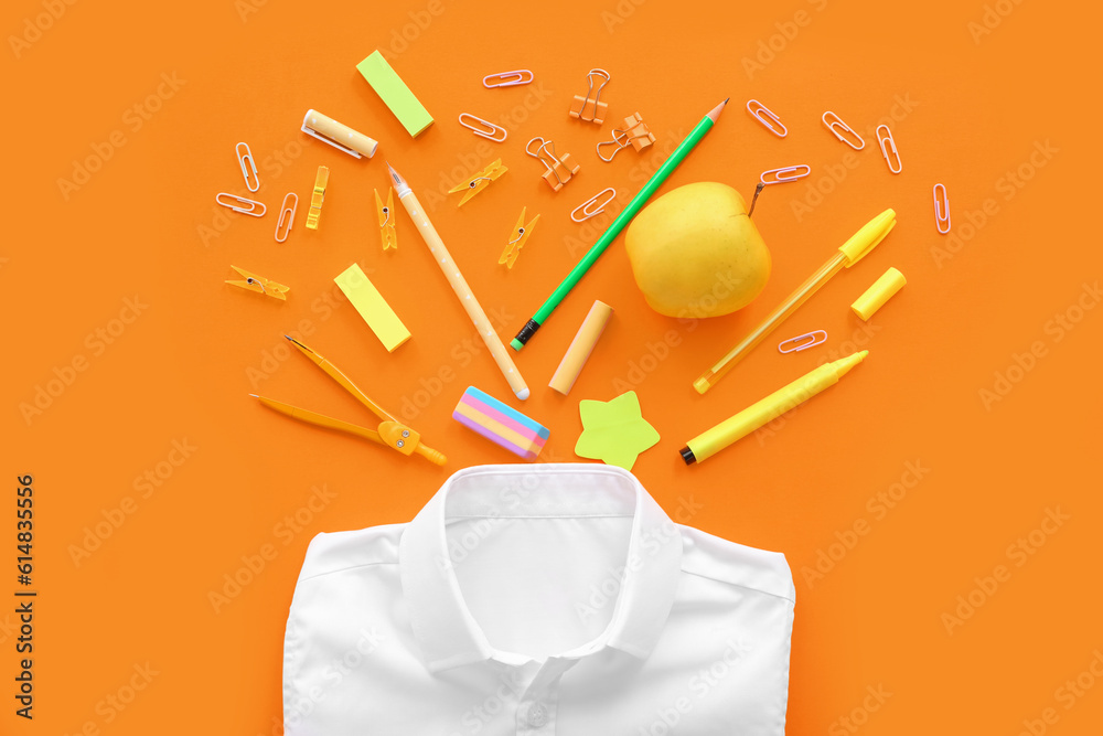 School shirt with fresh apple and different stationery on orange background