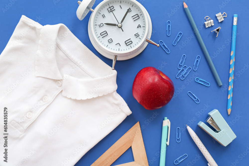 Shirt with red fresh apple, alarm clock and different stationery on blue background