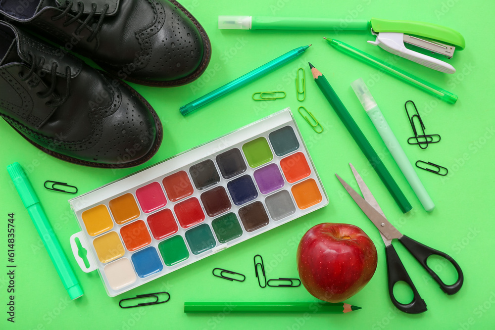 Shoes with fresh apple and different stationery on green background