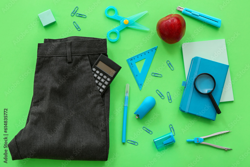 School pants with calculator fresh red apple and different stationery on green background