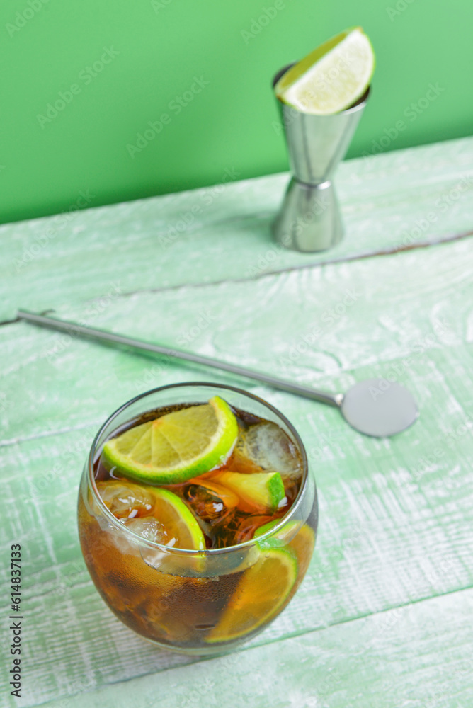 Glass of cold Cuba Libre cocktail on green wooden table