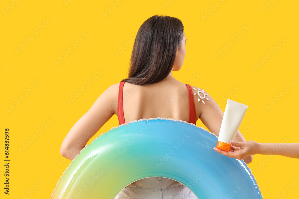 Young woman with sun made of sunscreen cream on her shoulder and inflatable ring against yellow back