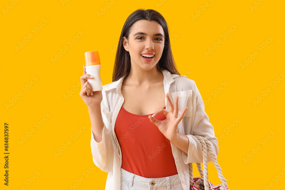 Young woman with sunscreen cream showing OK on yellow background