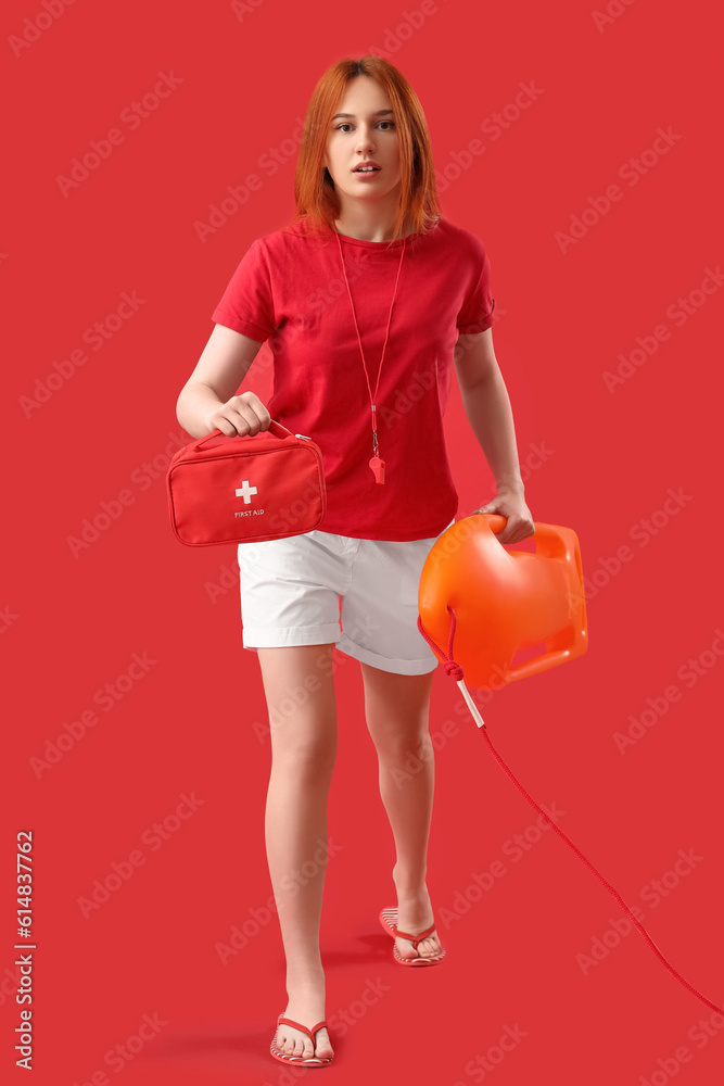 Female lifeguard with rescue buoy and first aid kit on red background