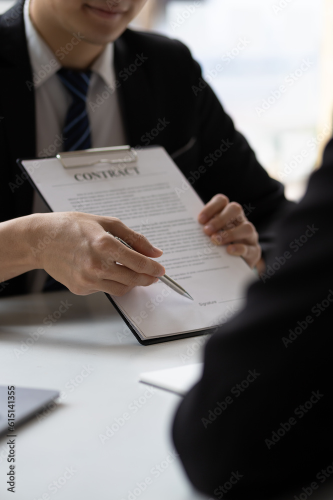 Real estate agent holding pen pointing at contract document for client to sign home purchase agreeme