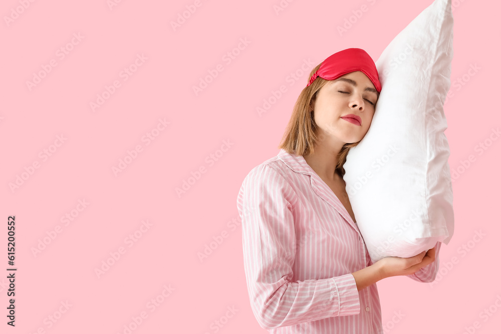 Young woman in pajamas with pillow sleeping on pink background