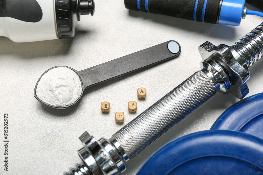 Scoop with amino acid supplement and sports equipment on light background, closeup