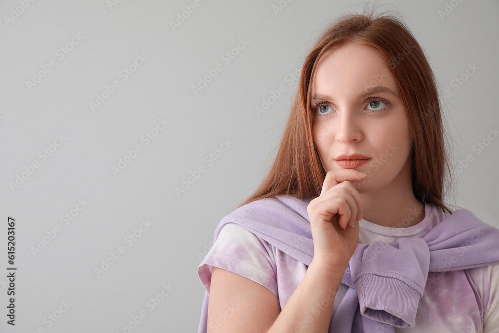 Thoughtful young redhead woman on grey background, closeup