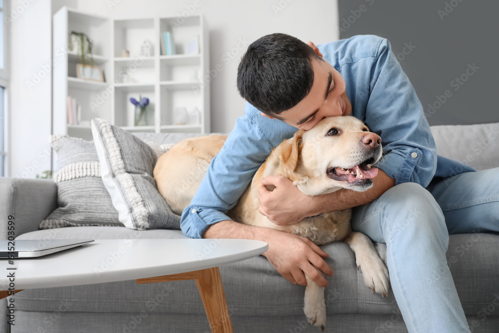 Young man with cute Labrador dog sitting on sofa at home