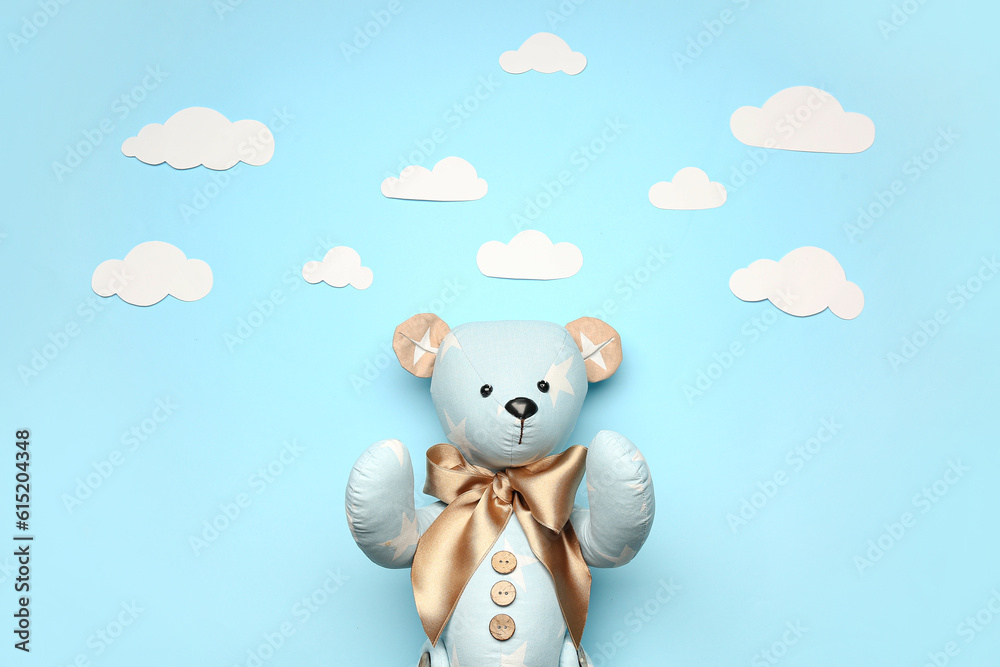 Toy bear with paper clouds on blue background