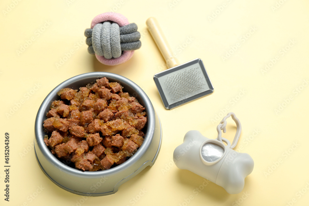 Bowl of wet pet food, grooming brush, ball and waste bags on color background