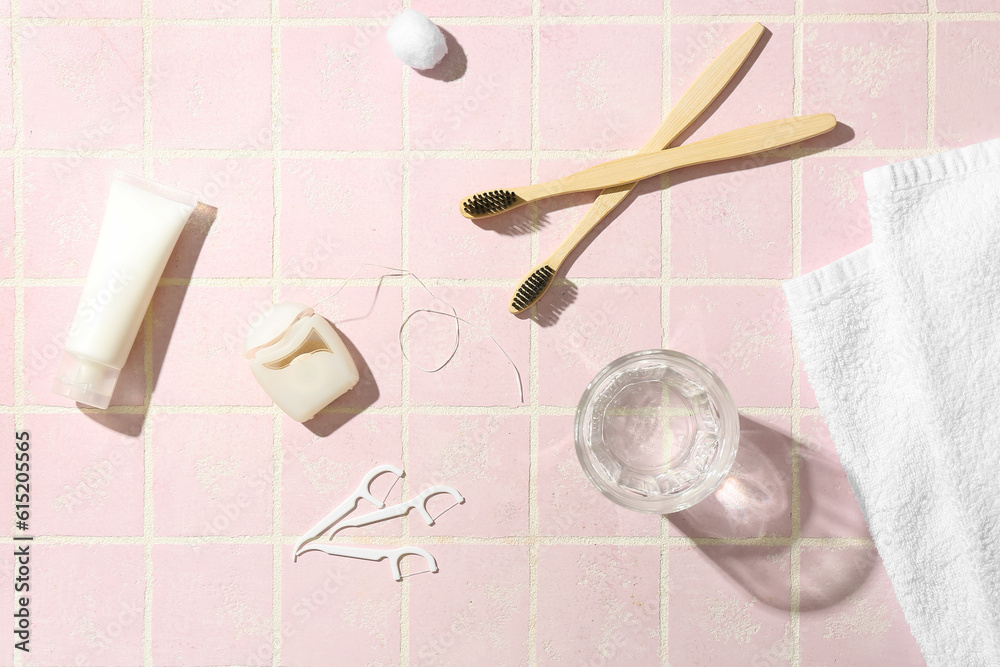 Dental floss, toothpicks, brushes, toothpaste and glass of water on pink tile table