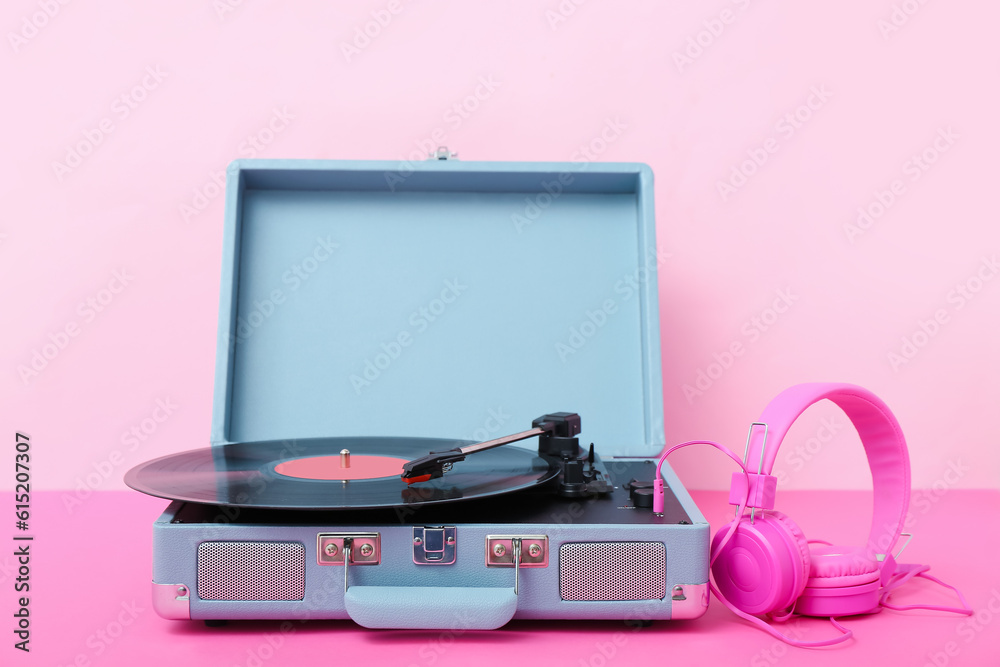 Record player with vinyl disk and headphones on table near pink wall