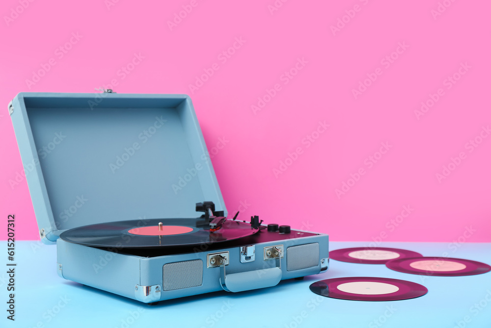 Record player with vinyl disks on table near pink wall