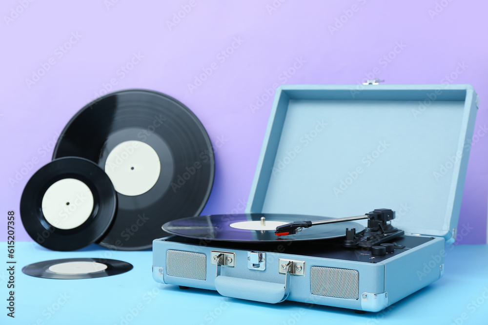 Record player with vinyl disks on table near lilac wall