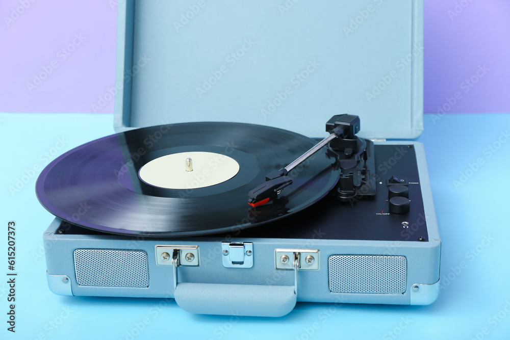 Record player with vinyl disk on table near lilac wall