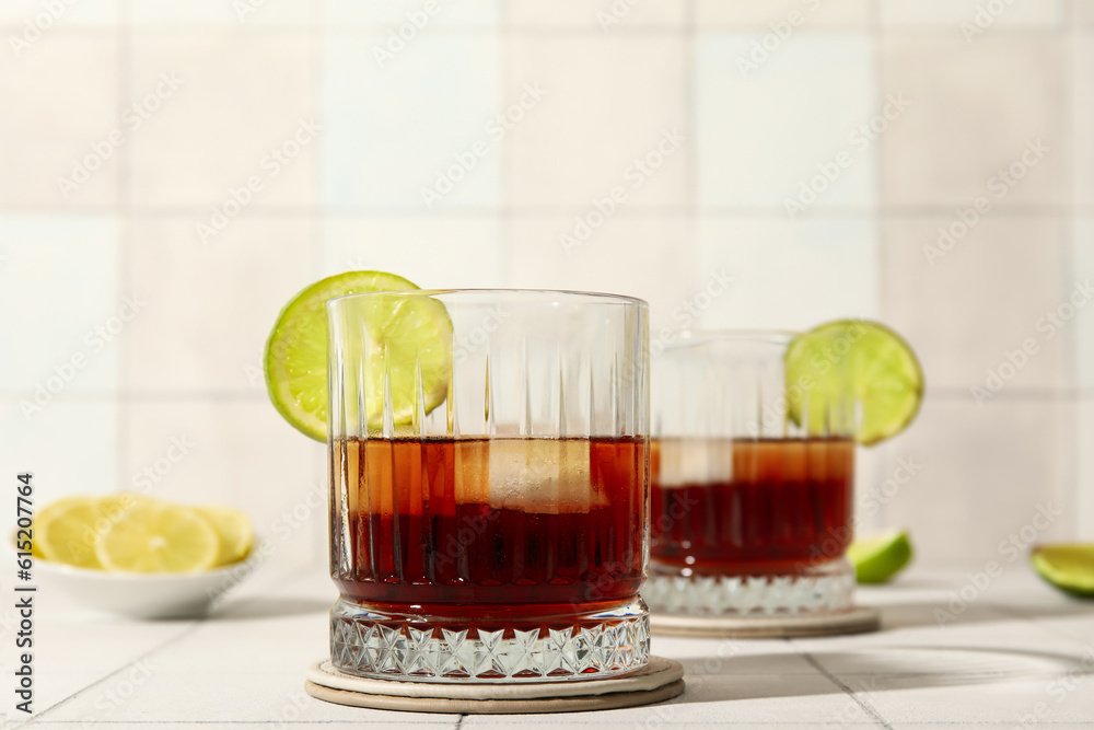 Glasses of cold rum with lime on white tile background