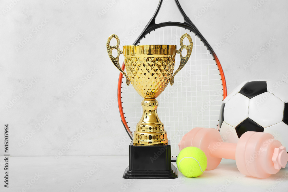 Gold cup with sports equipment on light background