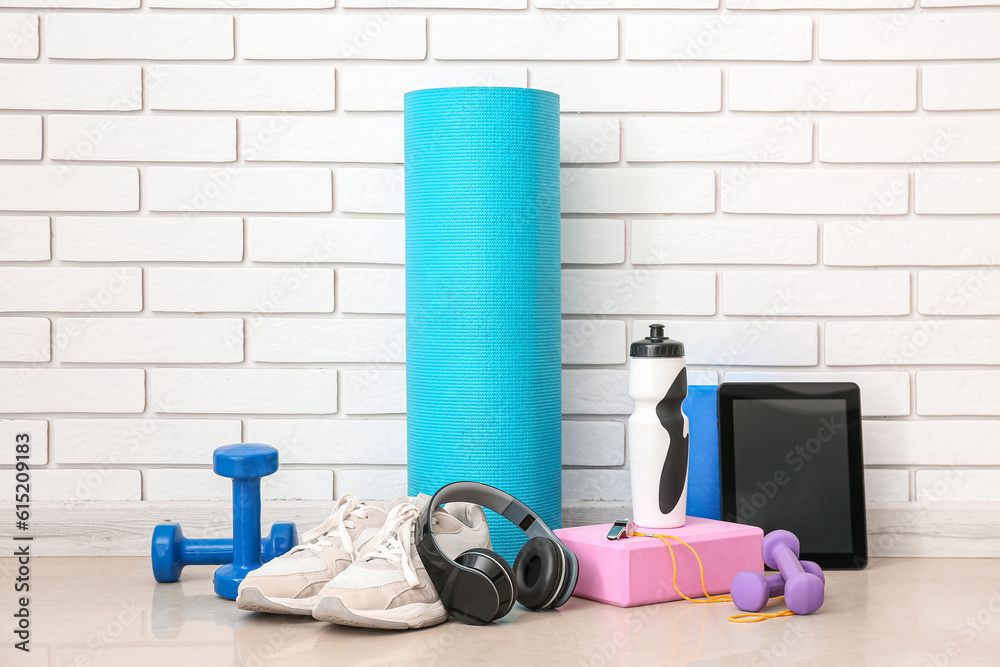 Sports equipment with headphones, tablet computer and bottle near white brick wall