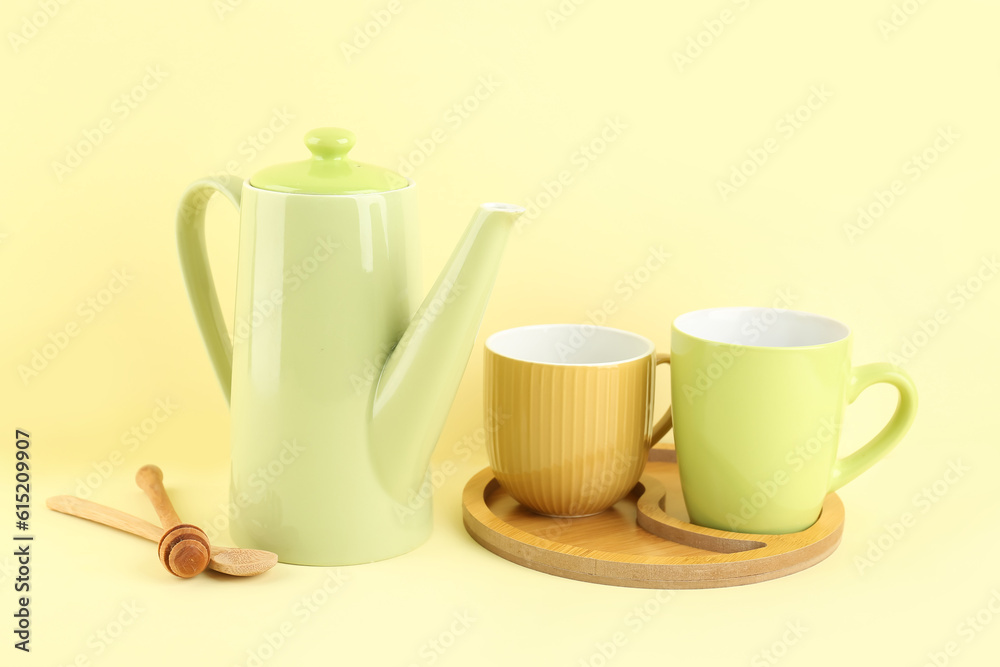 Teapot and tray with mugs on yellow background