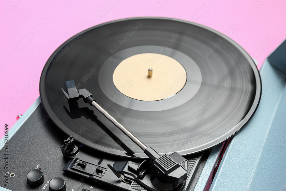 Record player with vinyl disk on pink background, closeup