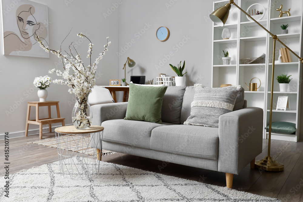 Interior of living room with grey sofa and blossoming tree branches on coffee table