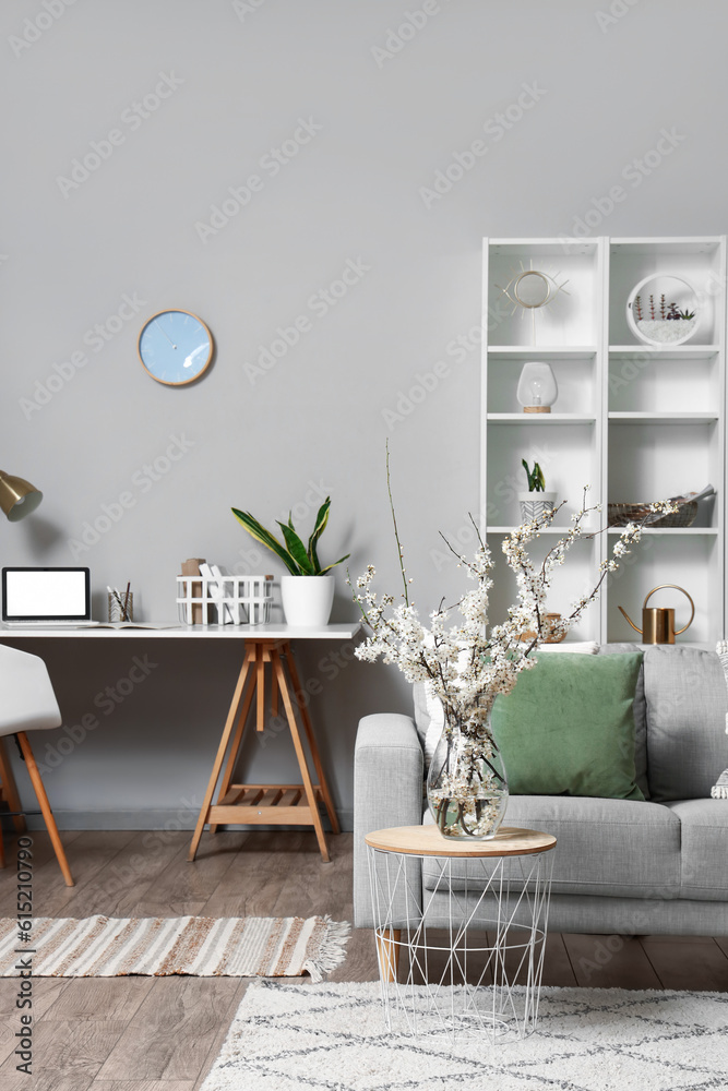 Interior of living room with grey sofa and blossoming tree branches on coffee table