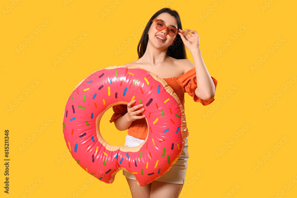 Young woman with inflatable ring in shape of doughnut on orange background