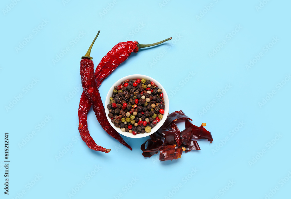 Bowl of peppercorns with dry hot chili peppers on blue background