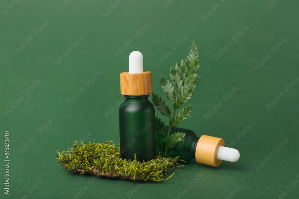 Bottles of cosmetic oil with plant twig and moss on green background