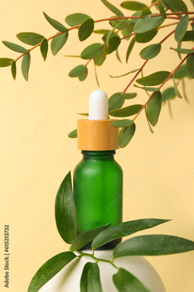 Bottle of cosmetic oil with eucalyptus twigs and stand on light yellow background