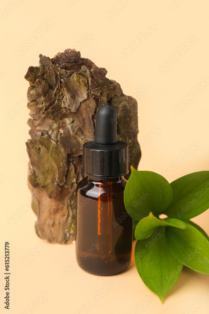 Bottle of cosmetic oil with plant twig and tree bark on beige background