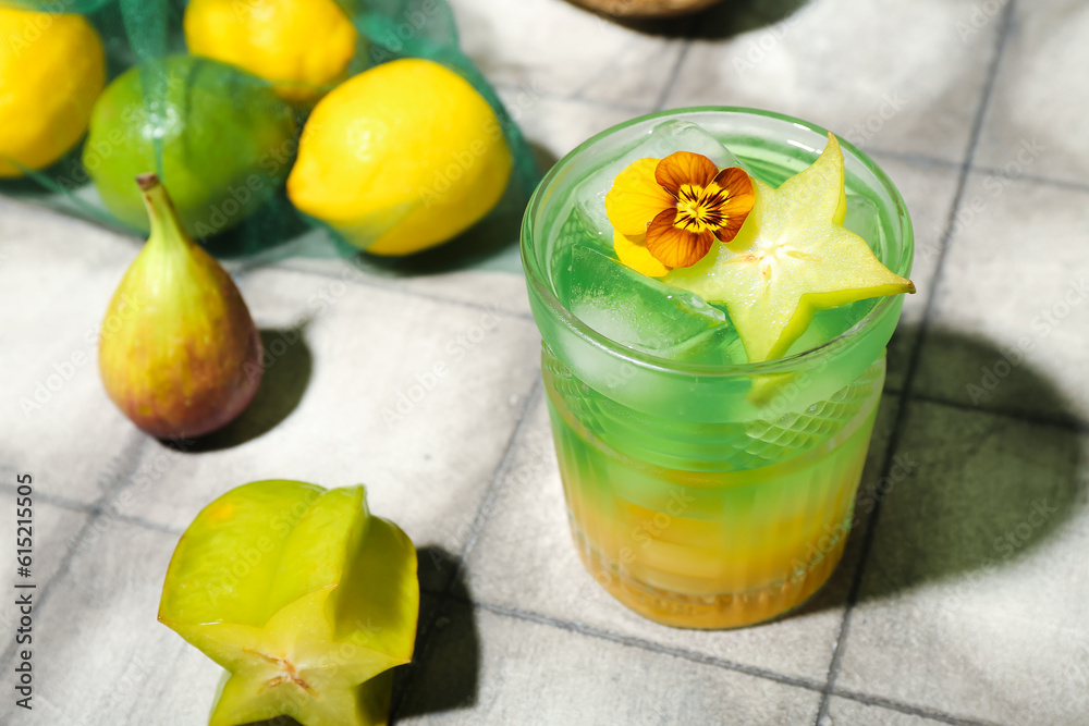 Fresh summer cocktail with carambola and flower on tile table