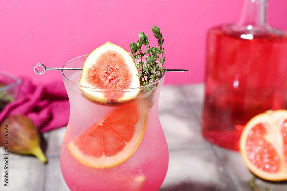 Fresh summer cocktail with fig, grapefruit and thyme on tile table near pink wall