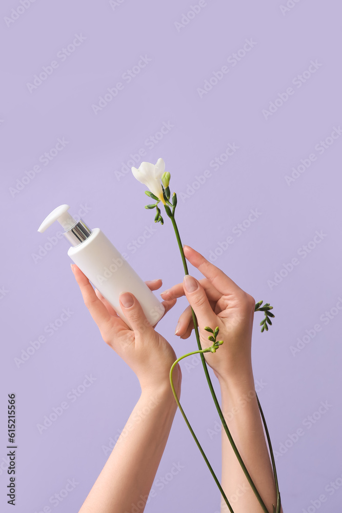 Hands holding bottle of cosmetic product and flower on lilac background