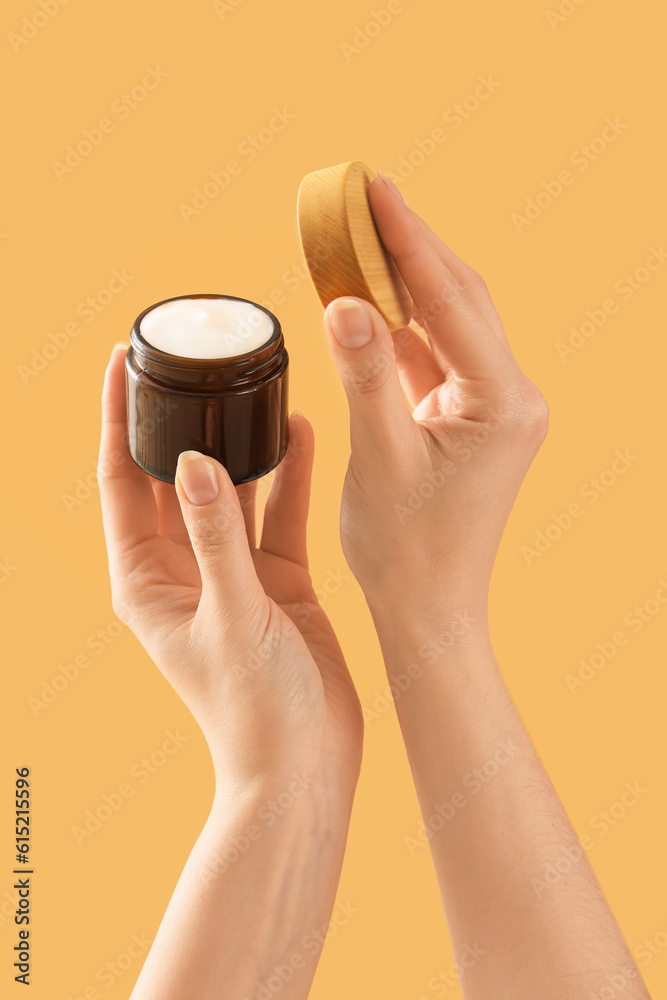 Hands holding cosmetic cream on beige background