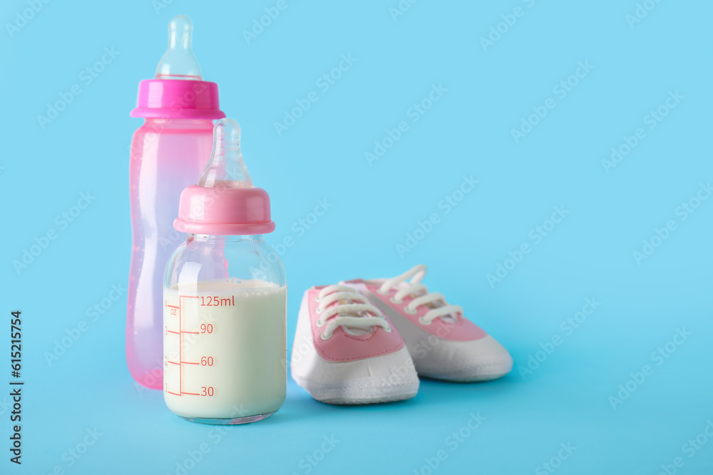 Bottles of milk for baby with booties on blue background