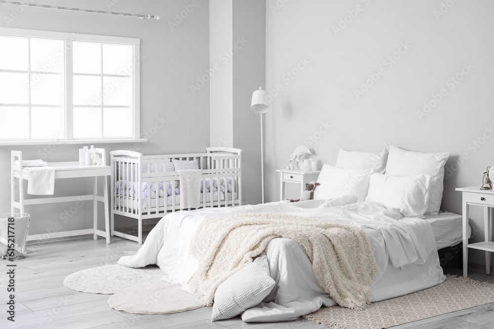 Interior of light bedroom with bed, changing table and baby crib