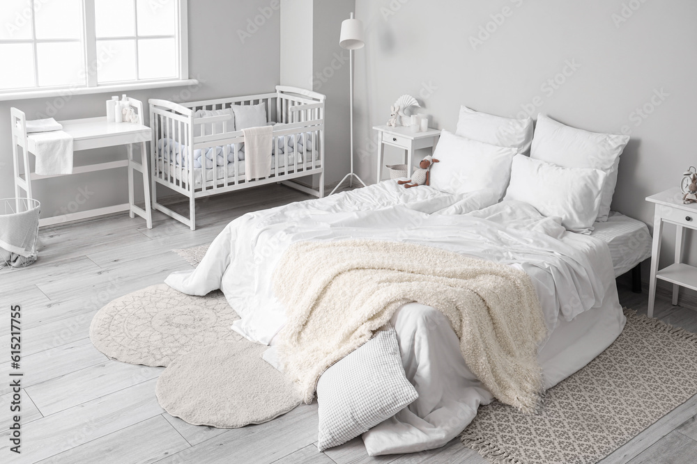 Interior of light bedroom with bed, changing table and baby crib