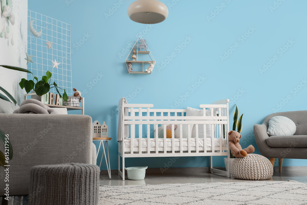 Interior of stylish bedroom with baby crib, sofa and armchair