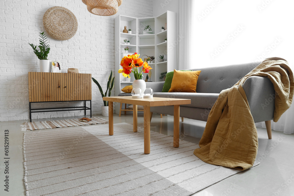 Interior of light living room with cozy grey sofa and tulip flowers on coffee table